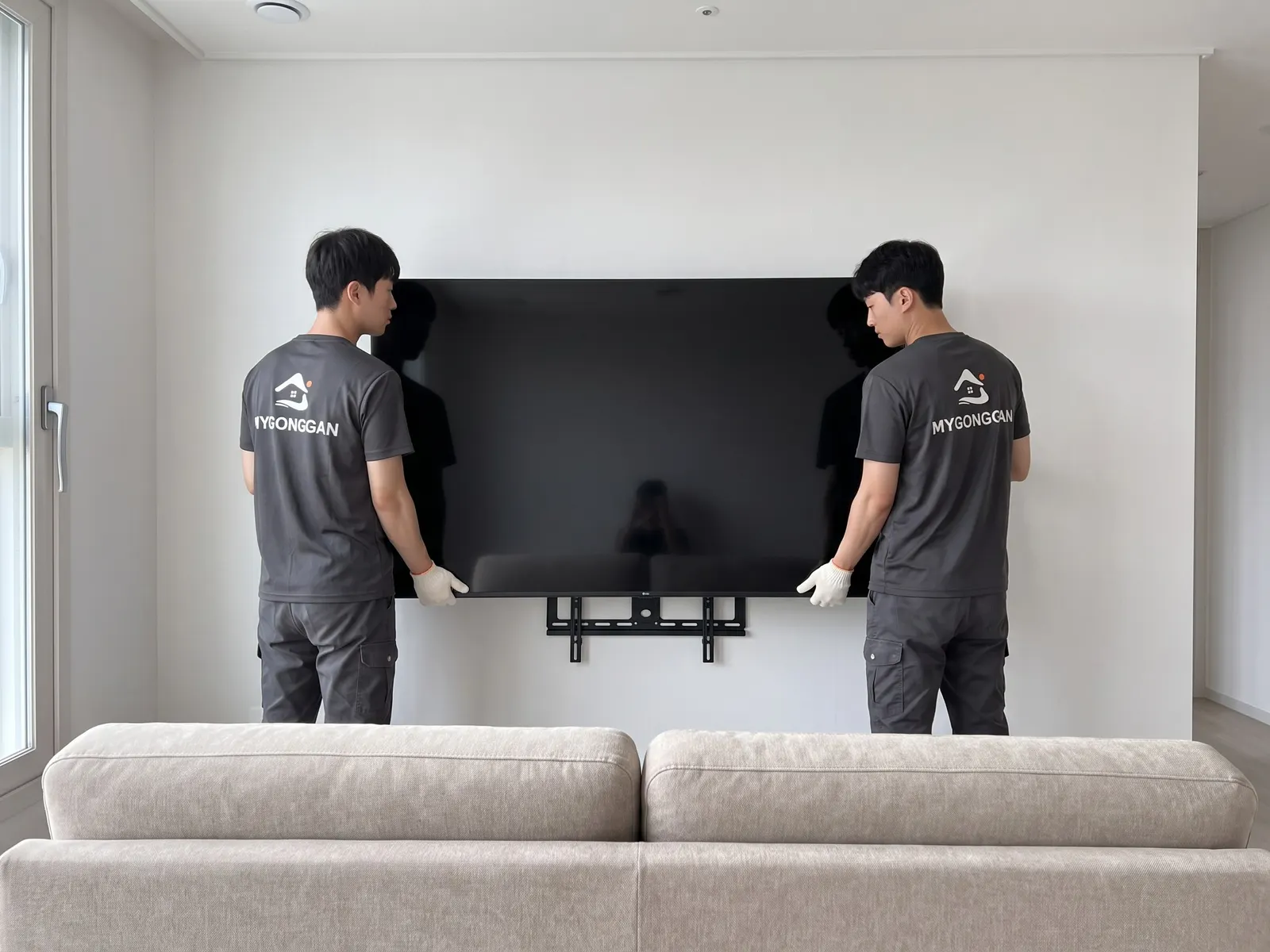 거실 벽 받침대에 대형 TV 를 함께 거는 작업자 두 명